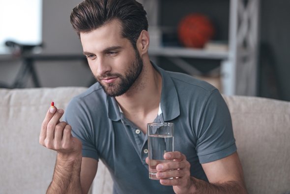 Young Man with a Pill and a Glass of Water in Hand